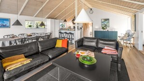 Ein modernes Wohnzimmer mit hoher Decke, einem Essbereich und einer Küche im Hintergrund.