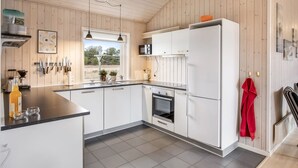 A modern kitchen with white cabinets, a large refrigerator, and a window with a view of greenery.
