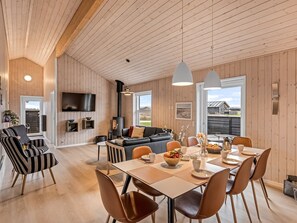 A spacious living area with a wooden ceiling, a black sofa, a dining table with chairs, and a television mounted on the wall. - "Elenore" - 900m from the sea by Interhome (Løkken)