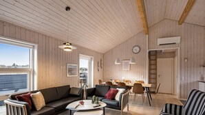 A spacious living area with a wooden ceiling, a dining table with chairs, a sofa, and a striped armchair.