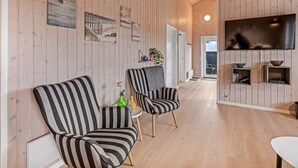 A spacious living area with striped armchairs, a flat-screen TV, and wooden paneling.