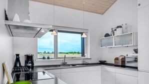Una cocina moderna con encimera negra, armarios blancos, un amplio ventanal con vistas y un cuenco verde sobre la encimera.