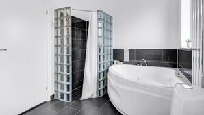 Un baño moderno con una bañera independiente, cabina de ducha con mampara de vidrio y paredes cubiertas de azulejos oscuros.