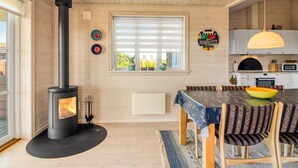 A modern kitchen with a wood-burning stove, a dining area with a table and chairs, and a window with blinds. - "Armgard" - 300m from the sea by Interhome (Løkken)