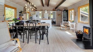 A spacious cabin interior with a dining area, kitchen, and a wood-burning stove.