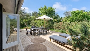An outdoor deck with a table and chairs, a lounge area with cushions, and a large umbrella.