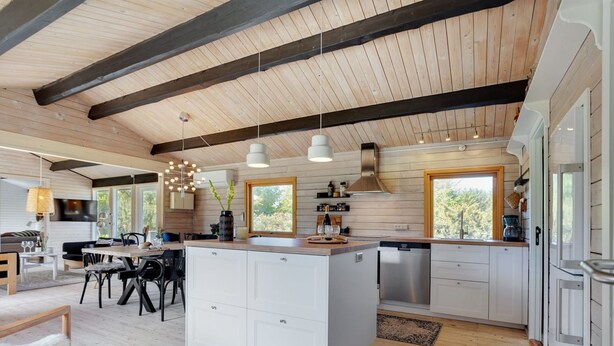 A modern kitchen with a central island, wooden beams on the ceiling, and large windows.