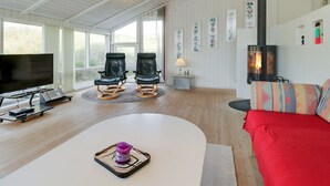 Ein geräumiges Wohnzimmer mit großem Fernseher, zwei Ledersesseln, einer Couch, einem Kamin und Kunstwerken an den Wänden.