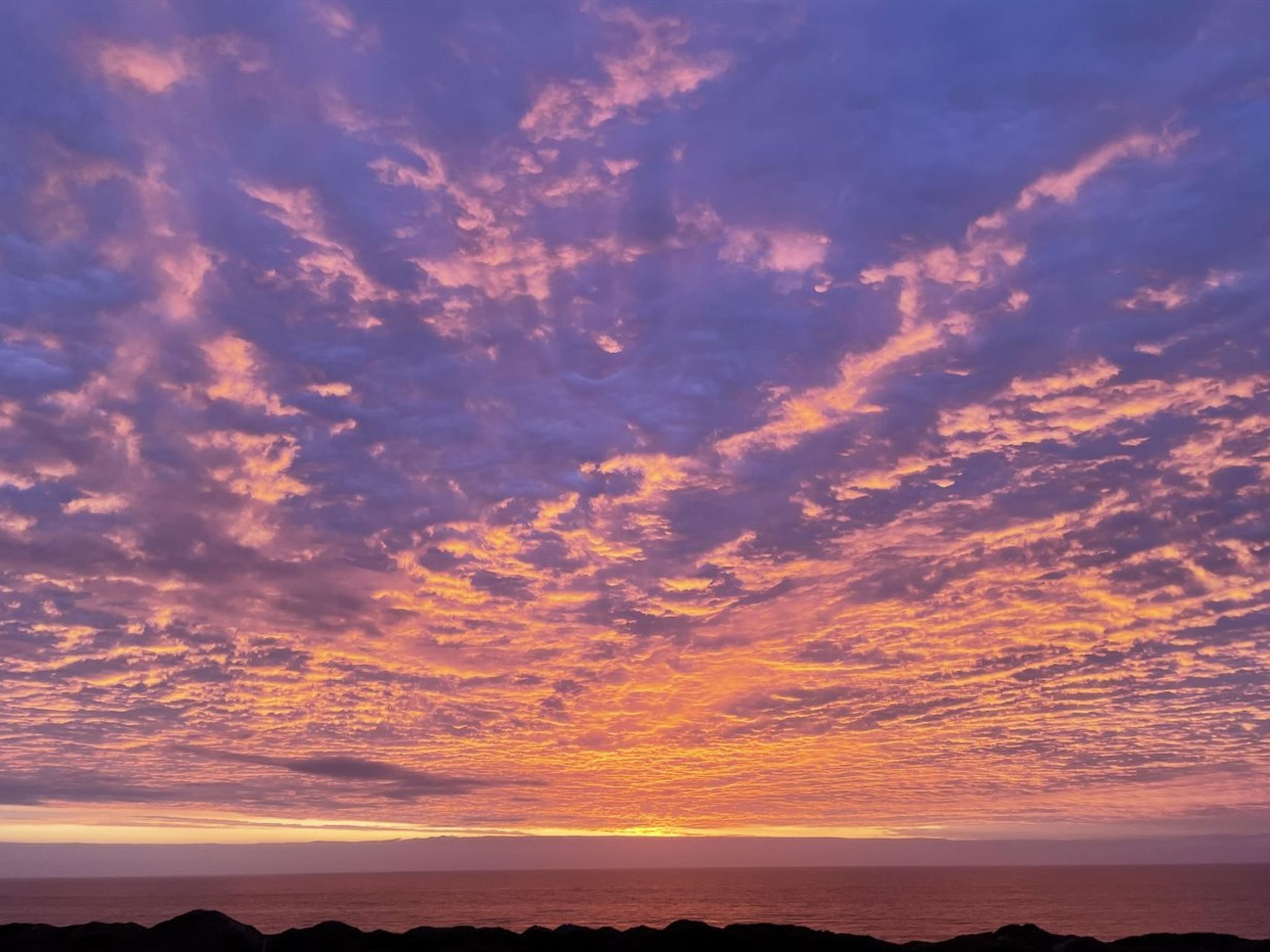 Un atardecer sobre el océano con un litoral rocoso.