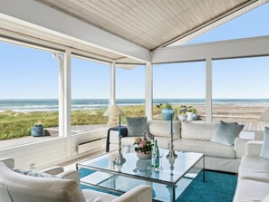 Una sala de estar con ventanales, una mesa de centro de vidrio, sofás blancos y vista a la playa.