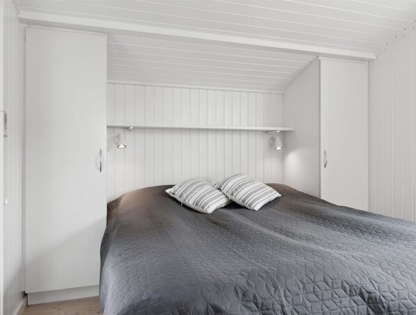 Un dormitorio con cama, dos almohadas, techo blanco y pared blanca.
