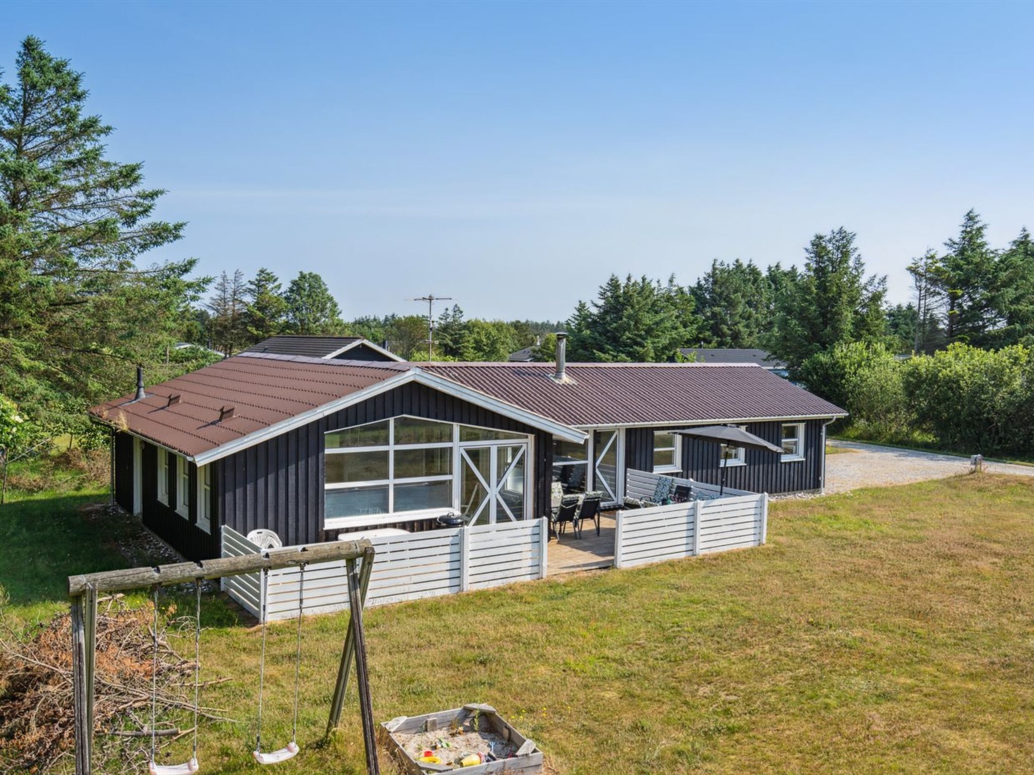 Une cabane à deux étages dotée d’un patio couvert, de grandes fenêtres et d’un toit en métal.