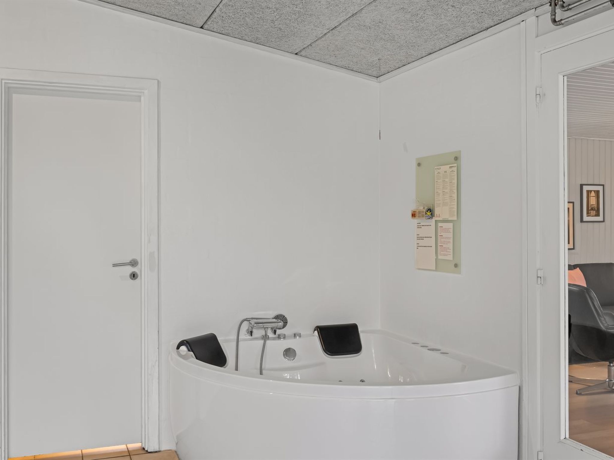 Une salle de bain avec une grande baignoire, une porte et un miroir dans lequel se reflète une chaise.
