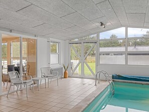 An indoor swimming pool area with a view of the outdoors, a seating area with chairs, and a tiled floor. - "Ingebore" - 700m from the sea by Interhome (Løkken)