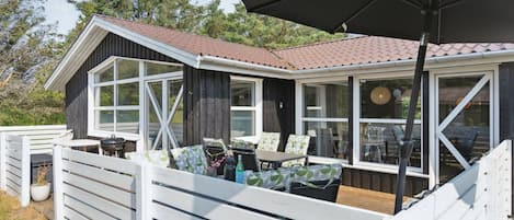 En stuga med en täckt uteplats, stora fönster och ett vitt staket.