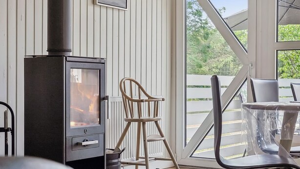 A cozy room with a wood-burning stove, a dining table with chairs, and a large window offering a view of the outdoors. - "Ingebore" - 700m from the sea by Interhome (Løkken)