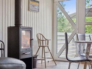 A cozy room with a wood-burning stove, a dining table with chairs, and a large window offering a view of the outdoors.