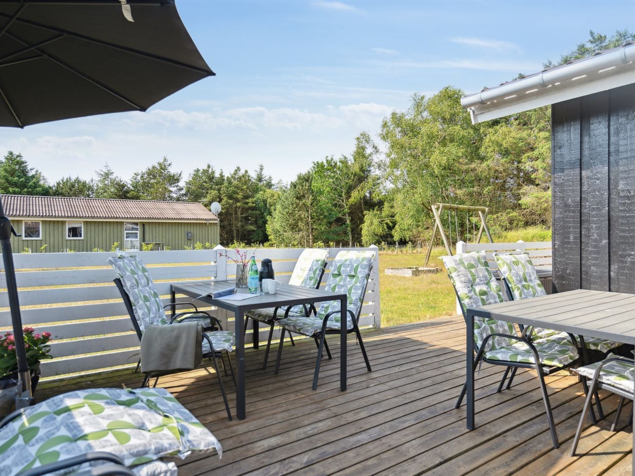 Eine Terrasse im Freien mit Holzboden, Metalltischen und -stühlen und einem großen Sonnenschirm, der Schatten spendet.