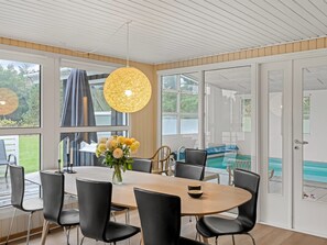 A dining area with a round table, black chairs, a vase with flowers, and a view of a swimming pool through glass doors. - "Ingebore" - 700m from the sea by Interhome (Løkken)