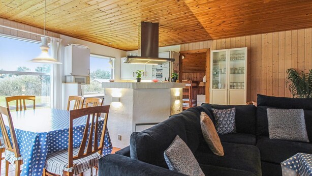 A cozy living room with a dark blue sofa, wooden dining table, and chairs. A kitchen area with a central island and cabinets is visible. - "Frellef" - 491m from the sea by Interhome (Løkken)