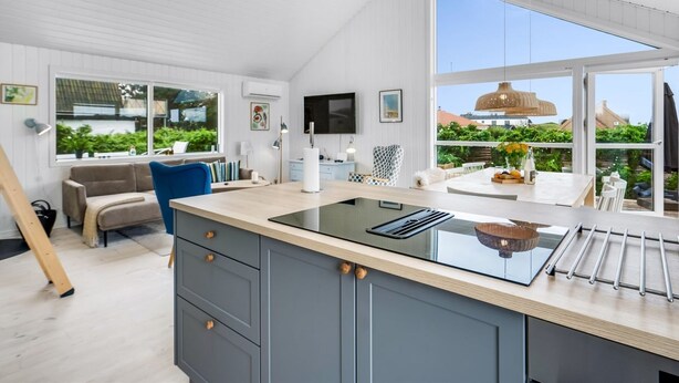 Une cuisine moderne dotée d’un grand îlot central, d’un coin repas avec une chaise bleue et d’une vue sur la verdure à l’extérieur.