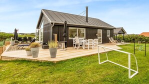 Une maison moderne dotée d’une terrasse en bois, d’un espace salon extérieur et d’une grande fenêtre donnant sur le jardin.