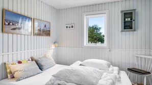 Une chambre à coucher comprenant un lit, une chaise, une fenêtre et des tableaux accrochés au mur.