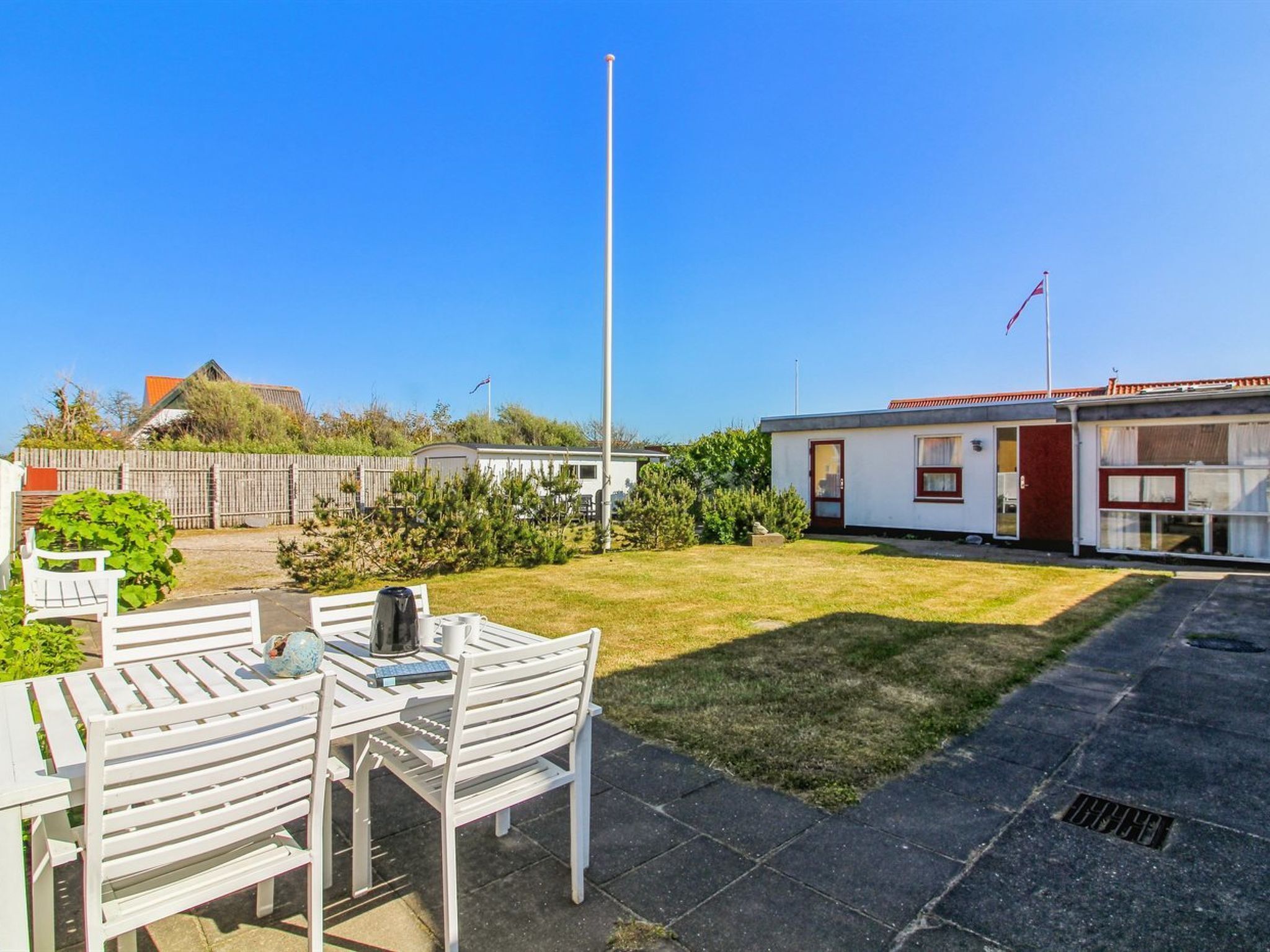 Et boligområde med et hvidt hus, et flagstang og en terrasse med et bord og stole.
