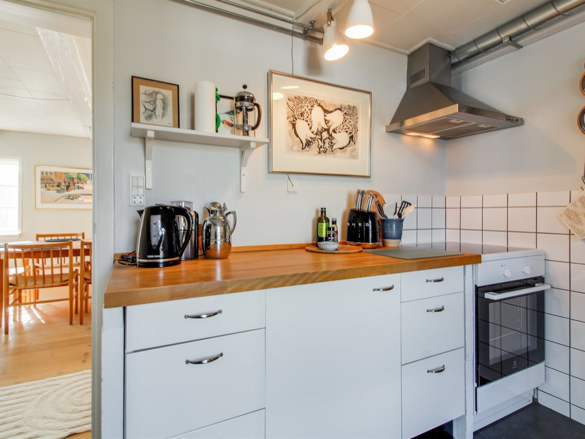 A modern kitchen with white cabinetry, a wooden countertop, a coffee maker, a kettle, and a built-in oven.