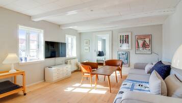 En moderne stue med et fladskærms-tv, et spiseområde med et træbord og stole, en sofa og en seng.