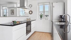 A modern kitchen with white cabinetry, a stainless steel range hood, a built-in oven, a black countertop, a window with a view, and a sink with a faucet.