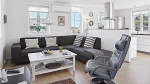 A modern living room with a sectional sofa, a coffee table, a leather chair, and a kitchen area with a sink and cabinets.
