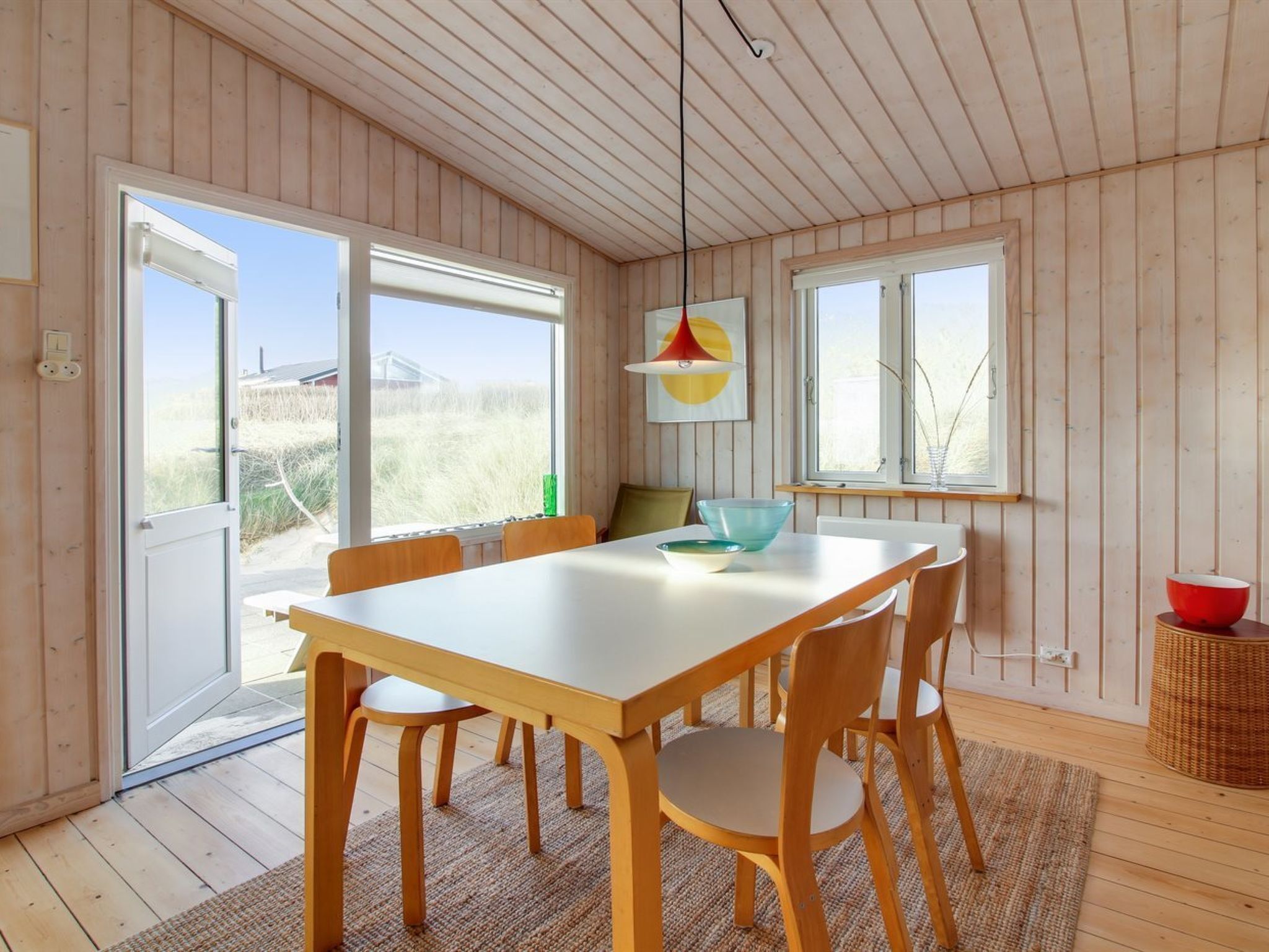 Een moderne eetruimte met een houten tafel en stoelen, grote ramen en uitzicht op het groen.