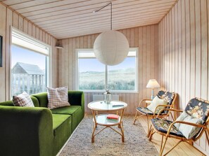 Une pièce avec un canapé vert, des chaises en osier, une table ronde et un luminaire suspendu.