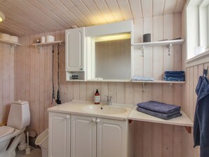 Une salle de bain avec un lambris en bois, un lavabo blanc, un miroir et des étagères où sont rangées des serviettes et des articles de toilette.