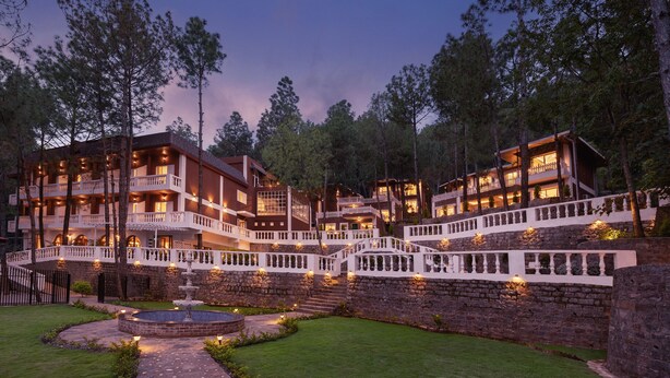 Un hotel de varios pisos con fachada de piedra, múltiples balcones y un patio central con una fuente.