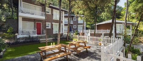 A courtyard with picnic tables, a white picket fence, and a red door on a brick building.