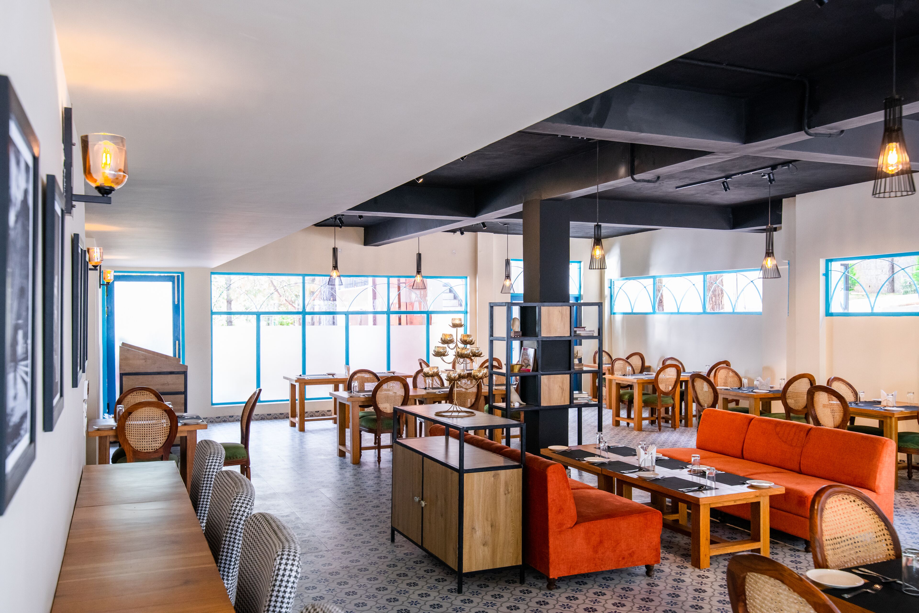 Un restaurante moderno con mobiliario de madera, una variedad de opciones de asientos y grandes ventanales que dejan entrar la luz natural.