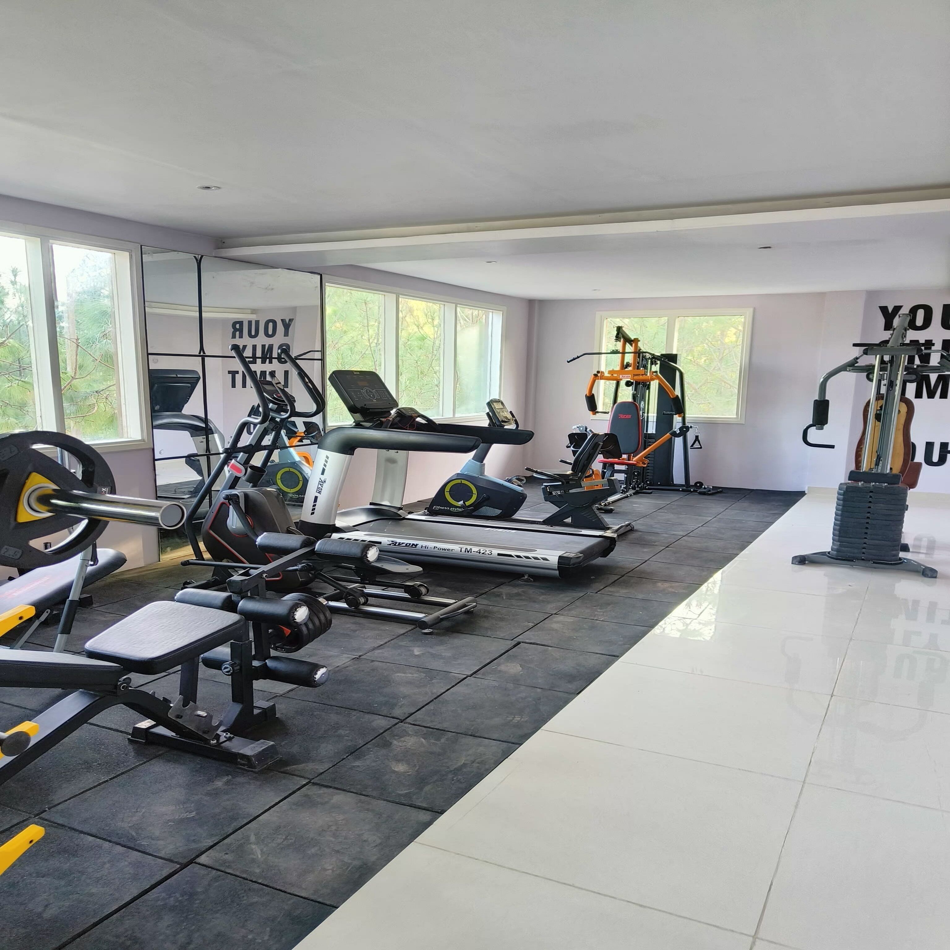 A modern gym with various exercise equipment, large windows, and motivational wall art.
