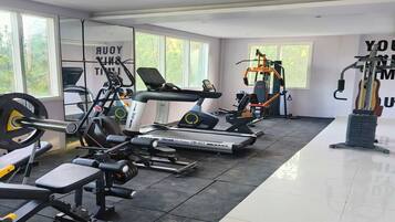 A modern gym with various exercise equipment, large windows, and motivational wall art.