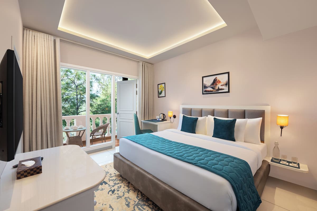 Ein Hotelzimmer mit einem großen Bett, einem Schreibtisch, einem Fernseher und einem Balkon mit Blick auf Bäume.