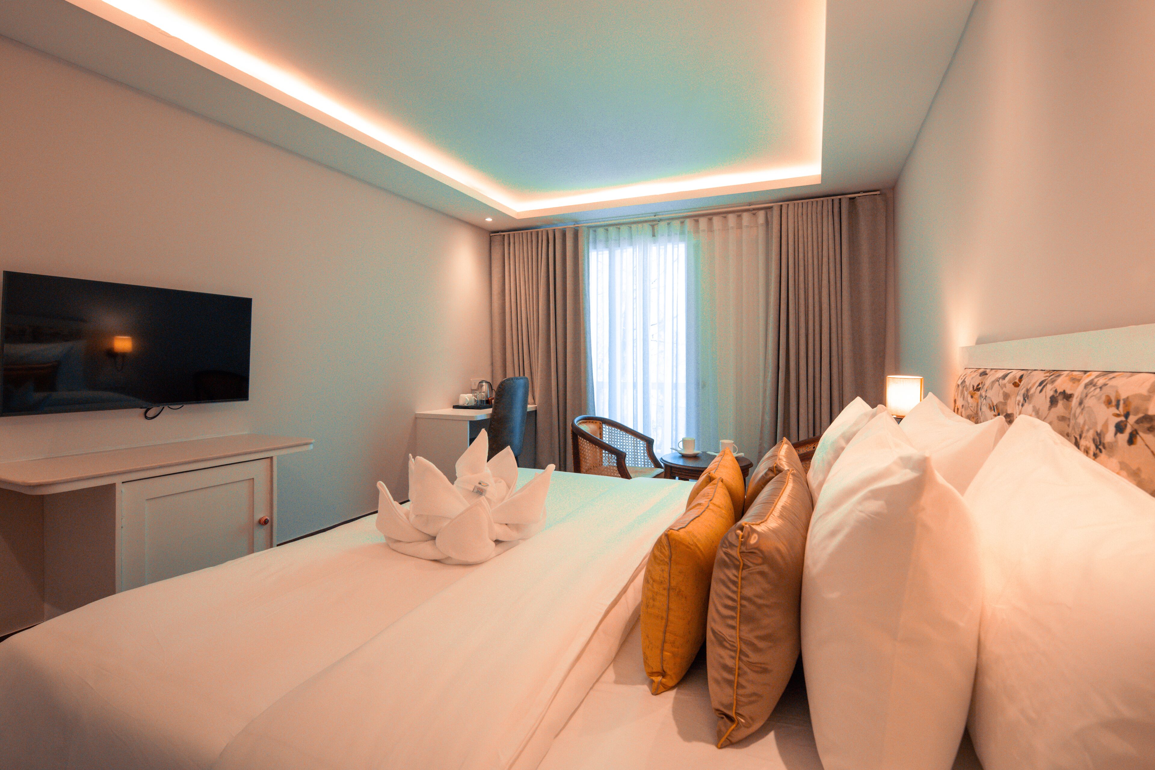 Une chambre d’hôtel équipée d’un lit, d’un bureau, d’une chaise, d’une télévision et d’une fenêtre avec des rideaux.