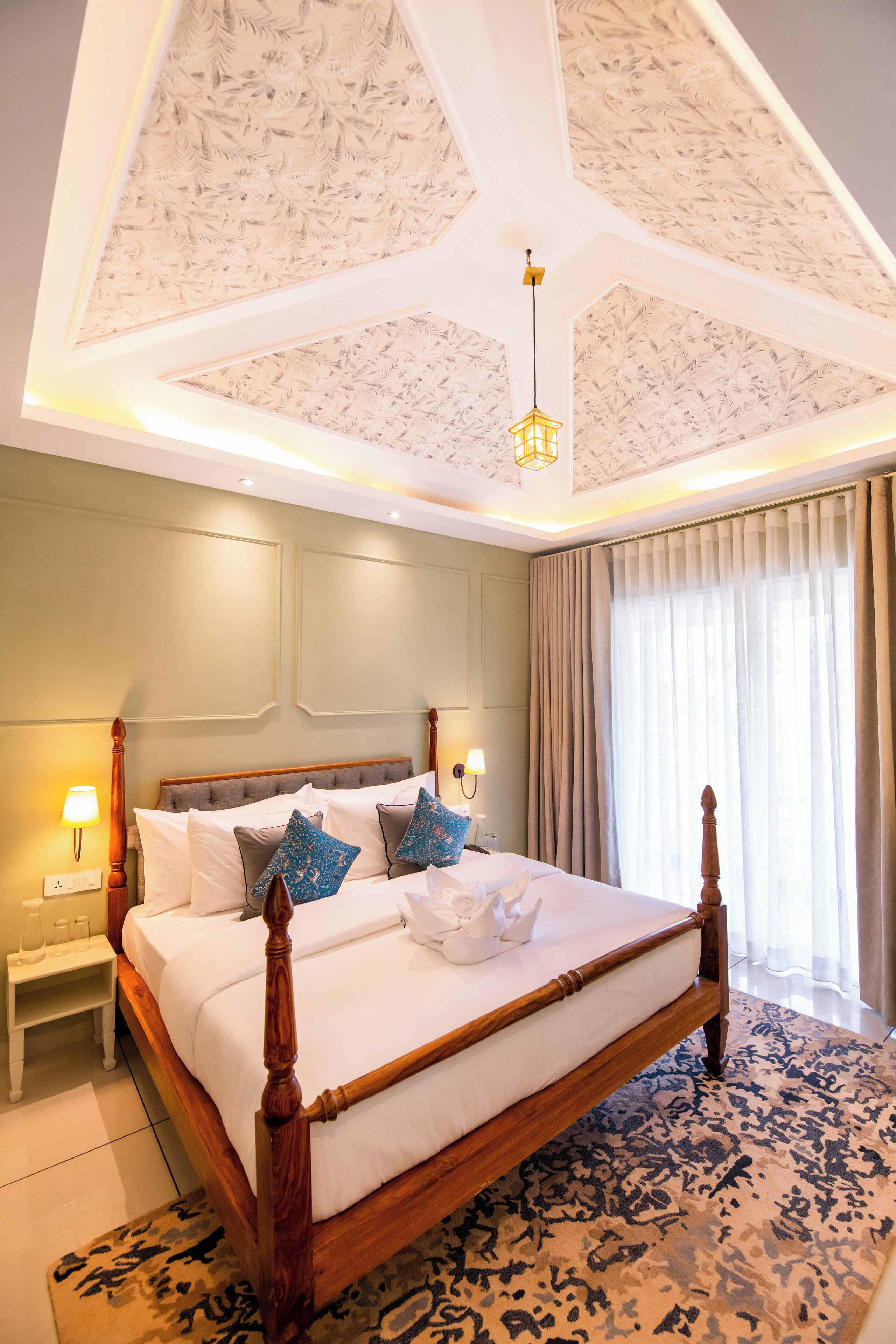 A hotel room with a large bed, a nightstand with a lamp, and a ceiling with a unique design.