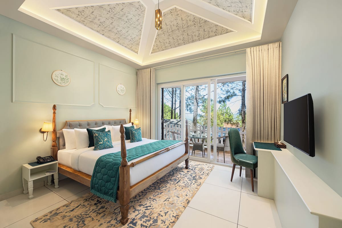 Ein Hotelzimmer mit einem großen Bett, einem Schreibtisch mit Stuhl, einem Fernseher und einem Balkon mit Blick auf Bäume.