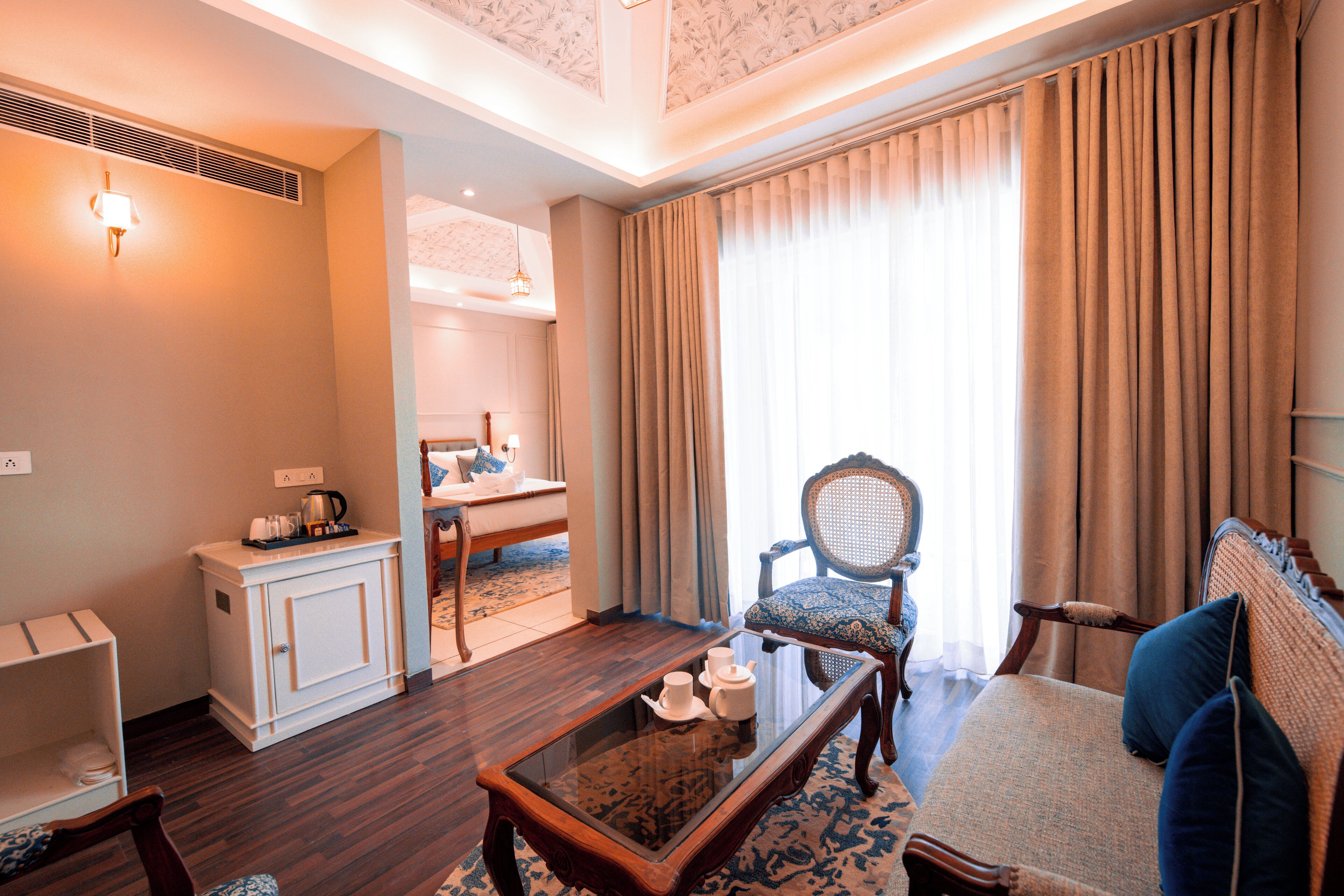 A hotel room with a dining area, a sofa, a chair, and a small table with a tray of items.
