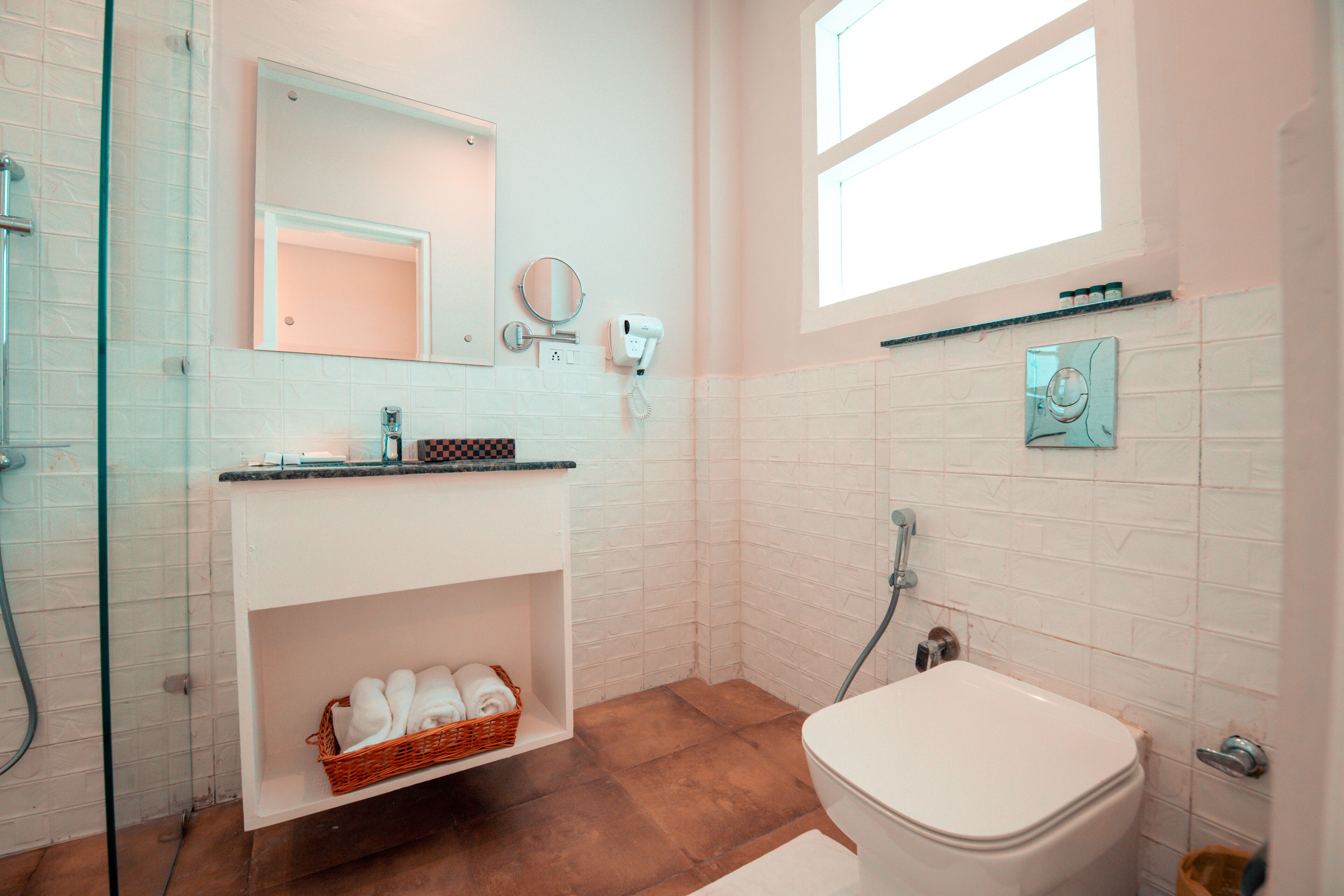 A modern bathroom with a glass shower enclosure, a white sink with a checkered soap dish, a mirror, and a white toilet.