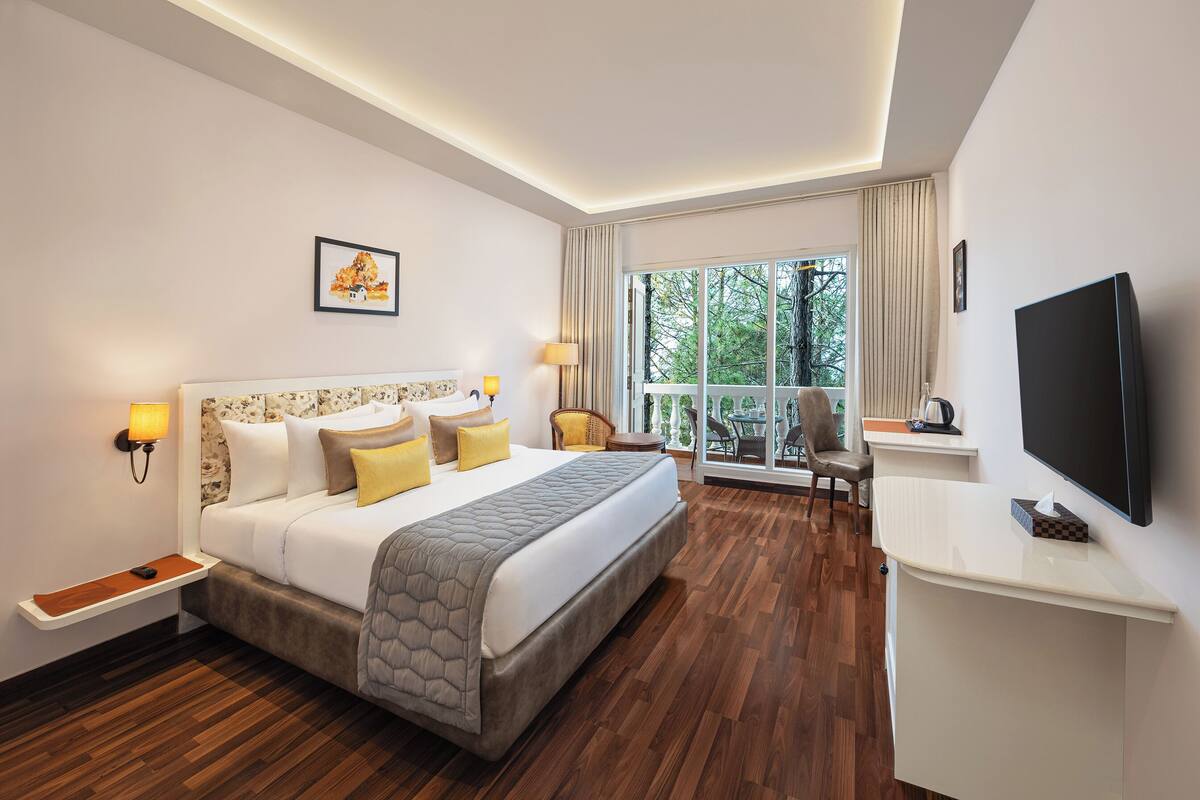 Ein Hotelzimmer mit einem großen Bett, Nachttischen, einem Fernseher und Blick ins Freie.