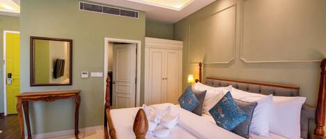 Una cama bien hecha con sábanas blancas y almohadones decorativos, una mesita de noche de madera y un espejo en la pared.