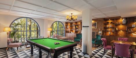 A pool table in a room with a checkered floor, a green pool table, and a billiards cue rack.