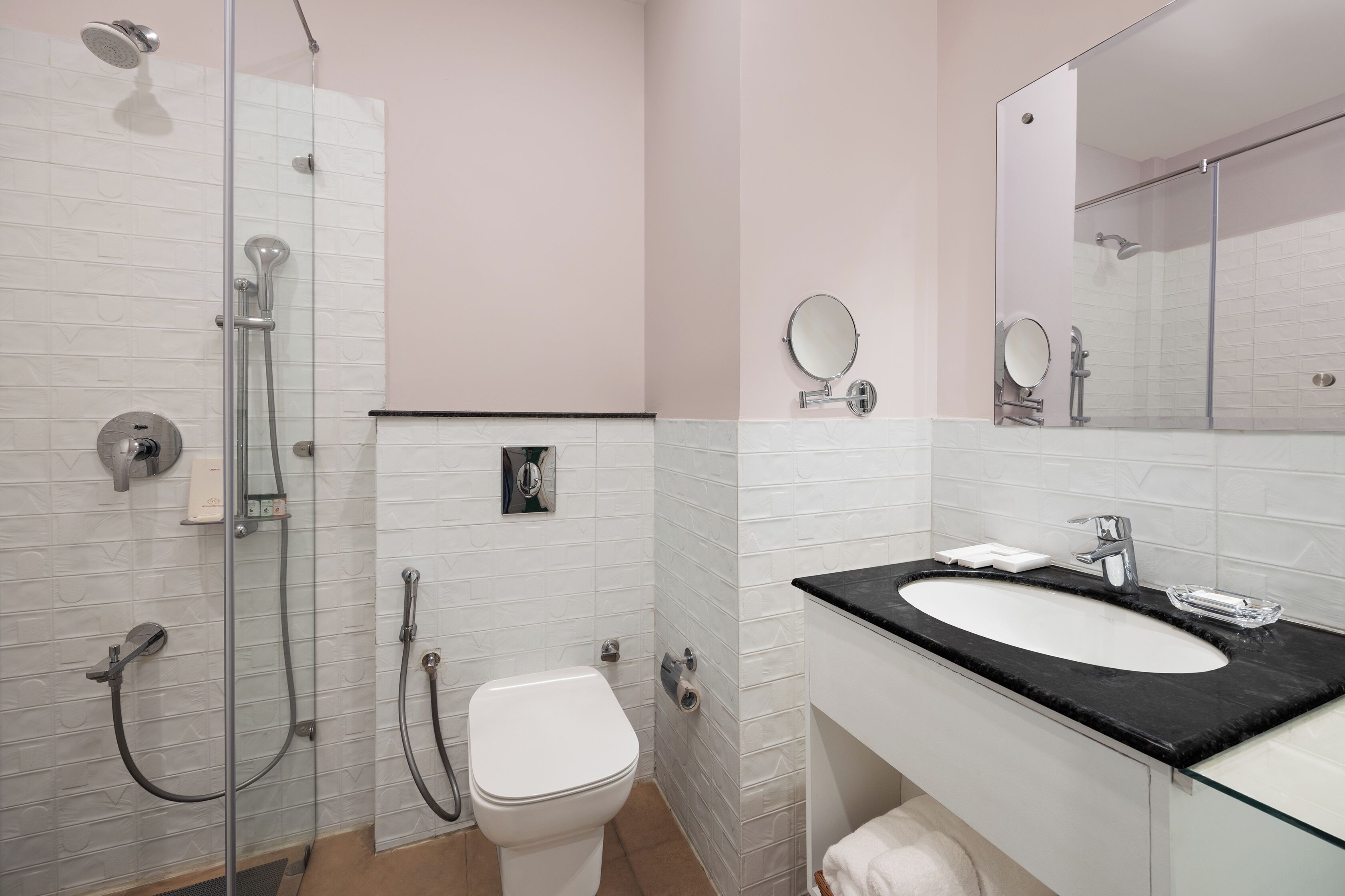 Un baño moderno con cabina de ducha de vidrio, un inodoro blanco, un lavabo negro con espejo y una pared con azulejos blancos.